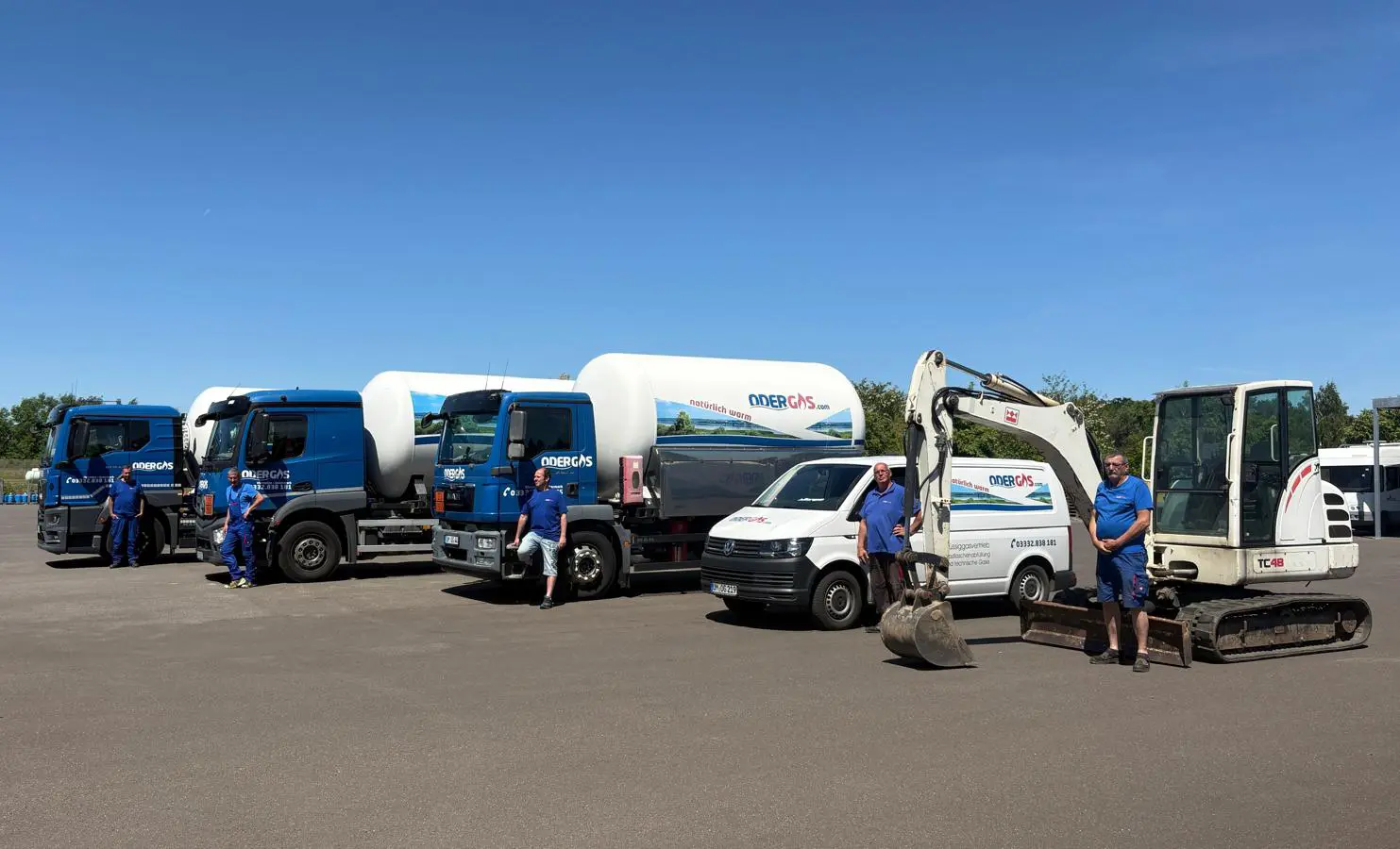 Bild des Fuhrparks und vier Mitarbeitern. Darauf zu sehen sind mehrere Tankwägen und andere Wägen.